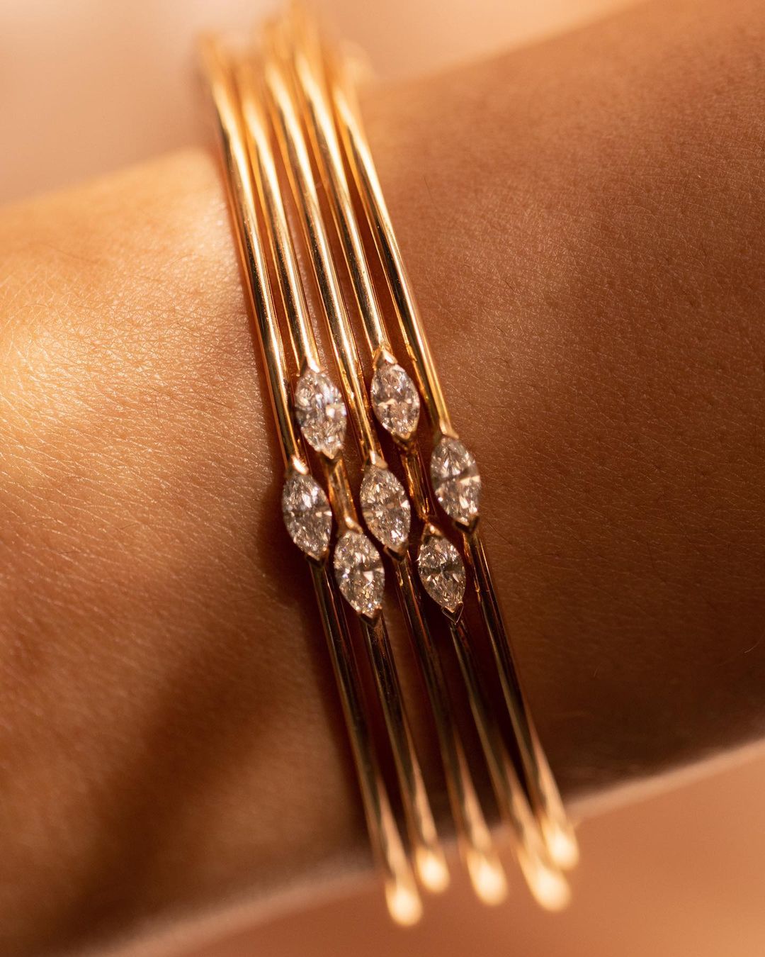Close-up of a woman's wrist adorned with multiple delicate gold bangles, each embellished with shimmering diamonds.