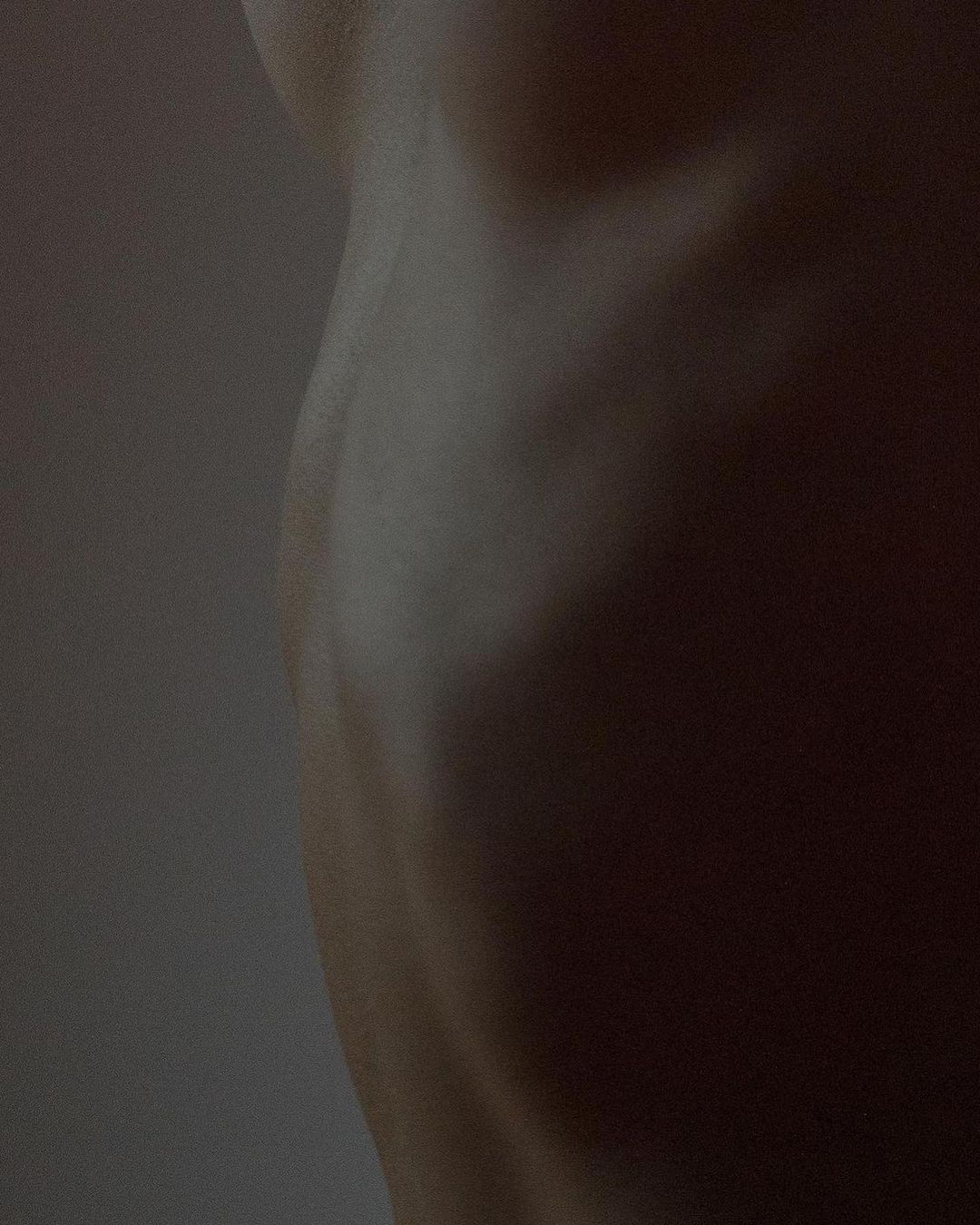 Close-up image of the side torso of an adult human figure. The skin is pale and lit softly to show the contours of the body.