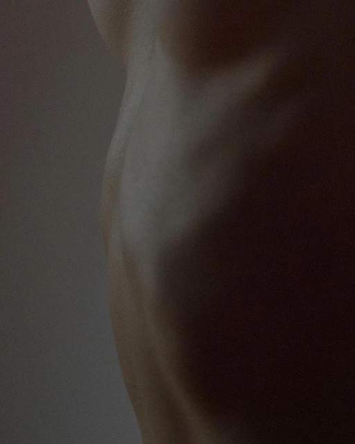 Close-up image of the side torso of an adult human figure. The skin is pale and lit softly to show the contours of the body.