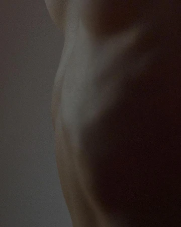 Close-up image of the side torso of an adult human figure. The skin is pale and lit softly to show the contours of the body.