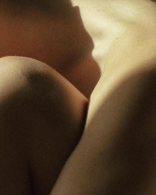 Close-up shot of a nude adult female, with visible shoulder, chest, arm, and side. The image features dramatic lighting and shadows.