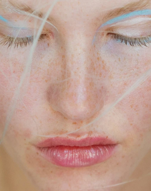 Close-up of a woman's face with eyes closed, freckles, and blue eye makeup, capturing a serene and artistic beauty concept.