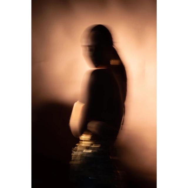 Abstract long exposure portrait of a female figure with dark hair wearing shimmering clothes, with a blurred background and soft studio lighting.