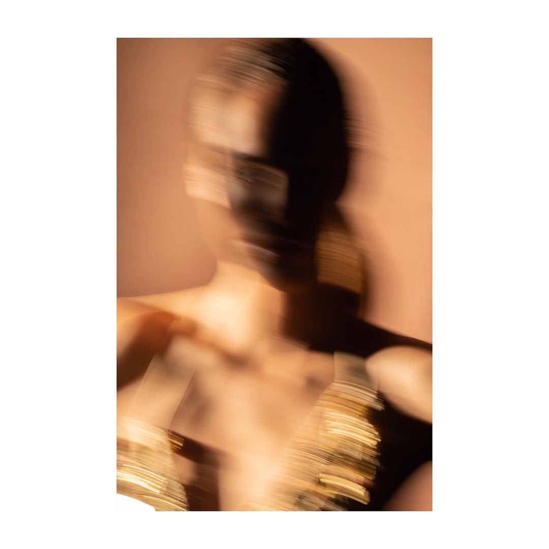 Blurred fashion photo of a dark-haired adult female model with painted face and metallic fabric. Stylish abstract beauty and design concept.