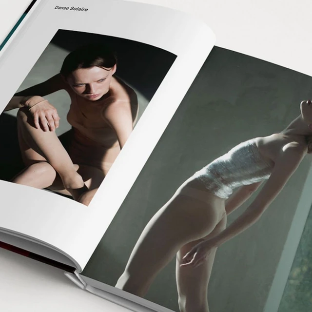Open book features two images of a slender woman with light skin in different poses against grey backdrops, bathed in warm sunlight.