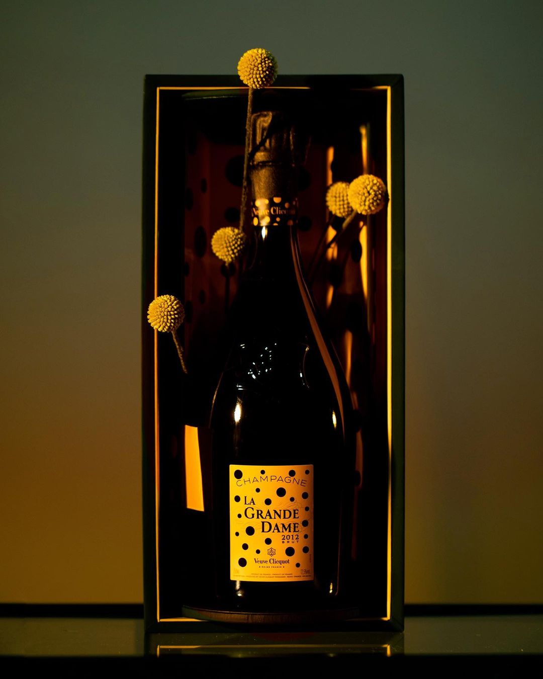 Elegant presentation of Veuve Clicquot La Grande Dame 2013 champagne in its box, accented with yellow craspedia flowers.