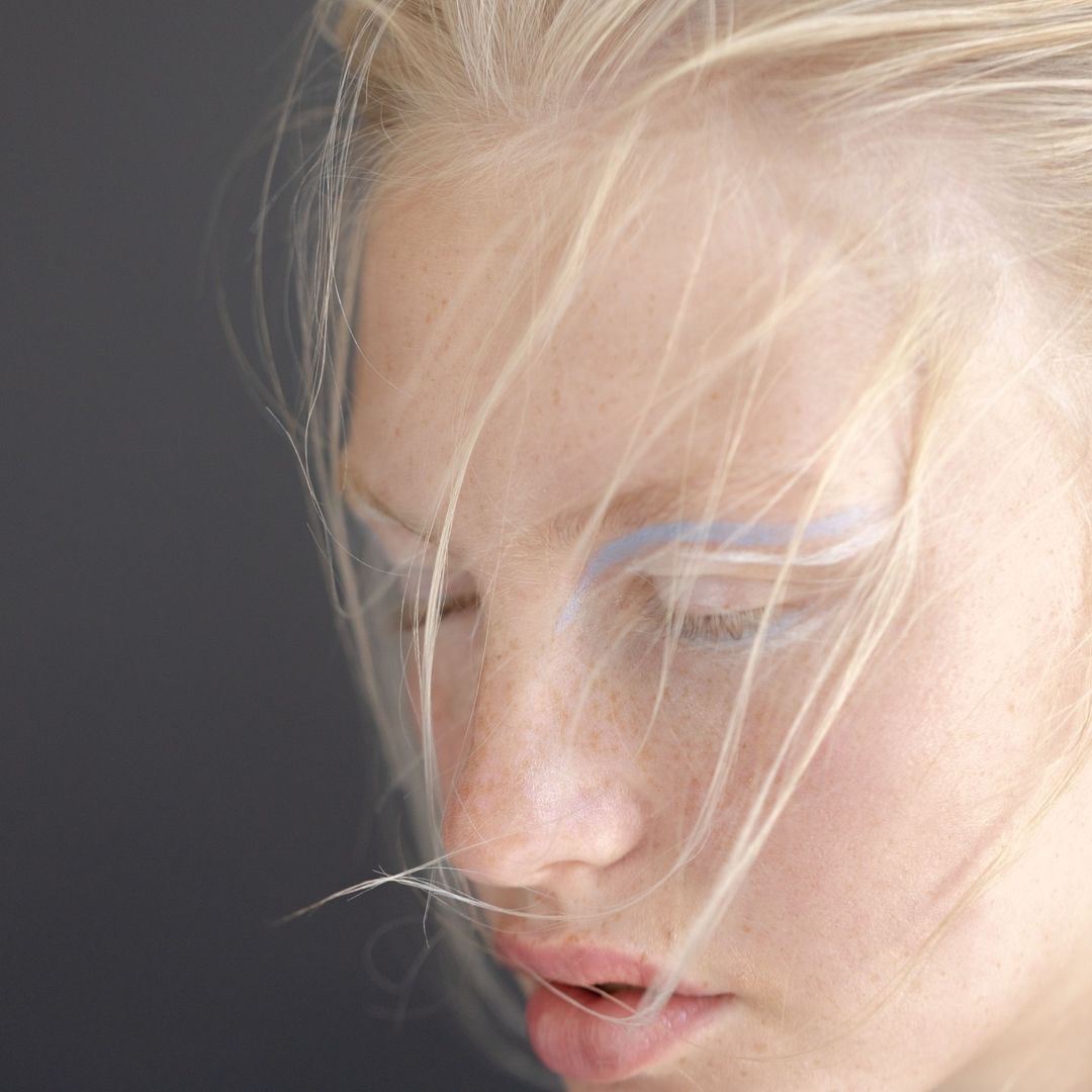 Close-up portrait of a woman with blonde hair, freckles, and light blue eye makeup by Laurent Castellani