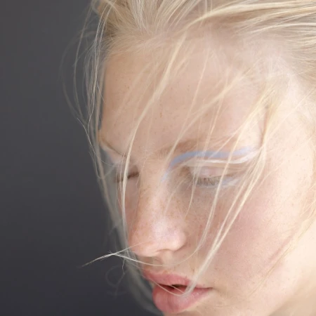 Close-up portrait of a woman with blonde hair, freckles, and light blue eye makeup by Laurent Castellani