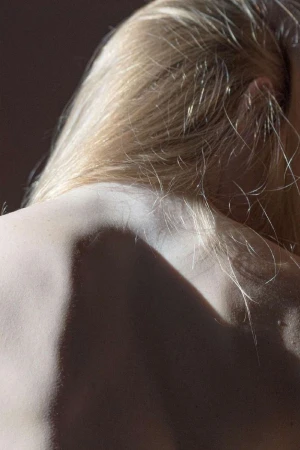 Close-up portrait of a woman's bare back and shoulder with long blonde hair, captured in directional light by Laurent Castellani