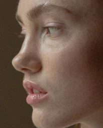Close-up profile portrait of a woman's face highlighting natural skin texture and freckles, photographed by Laurent Castellani.