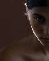 Close up portrait of a woman in low key lighting with a stark light beam across her face by Laurent Castellani