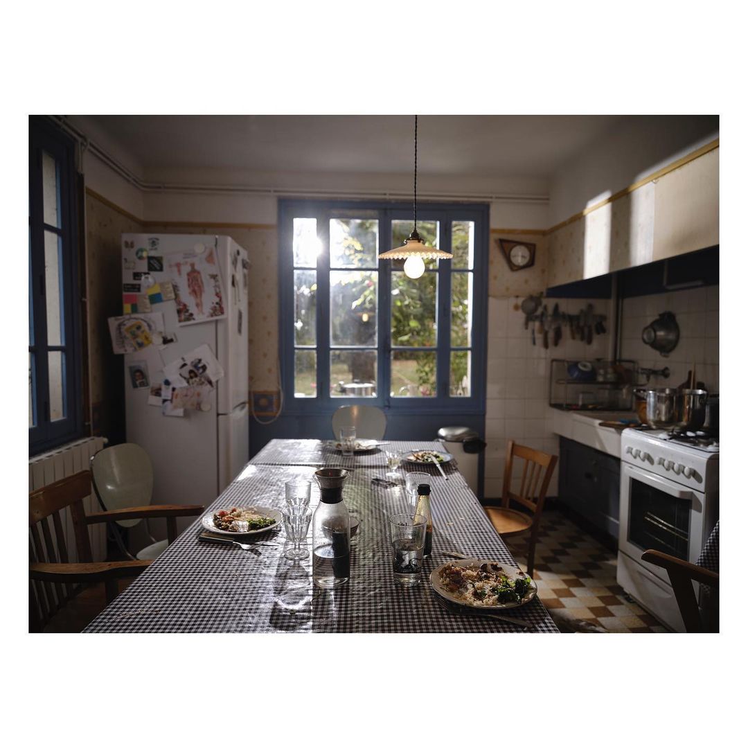 Dining room scene features a long table with a checkered tablecloth, set with plates, glasses, and food, under a hanging light fixture.