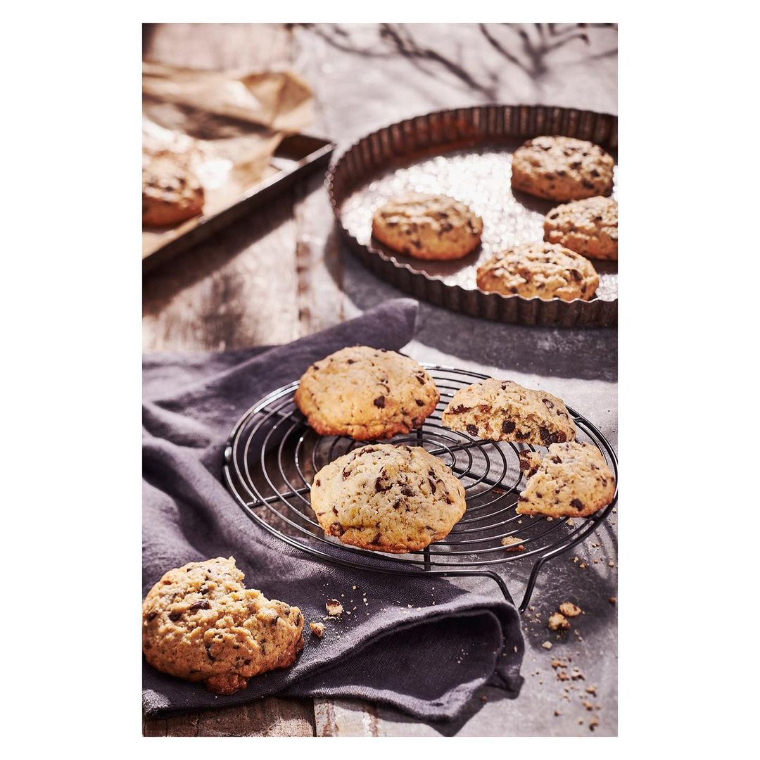 Overhead shot of chocolate chip cookies on a wire rack and in a baking pan, emphasizing fresh baked goods and natural light.
