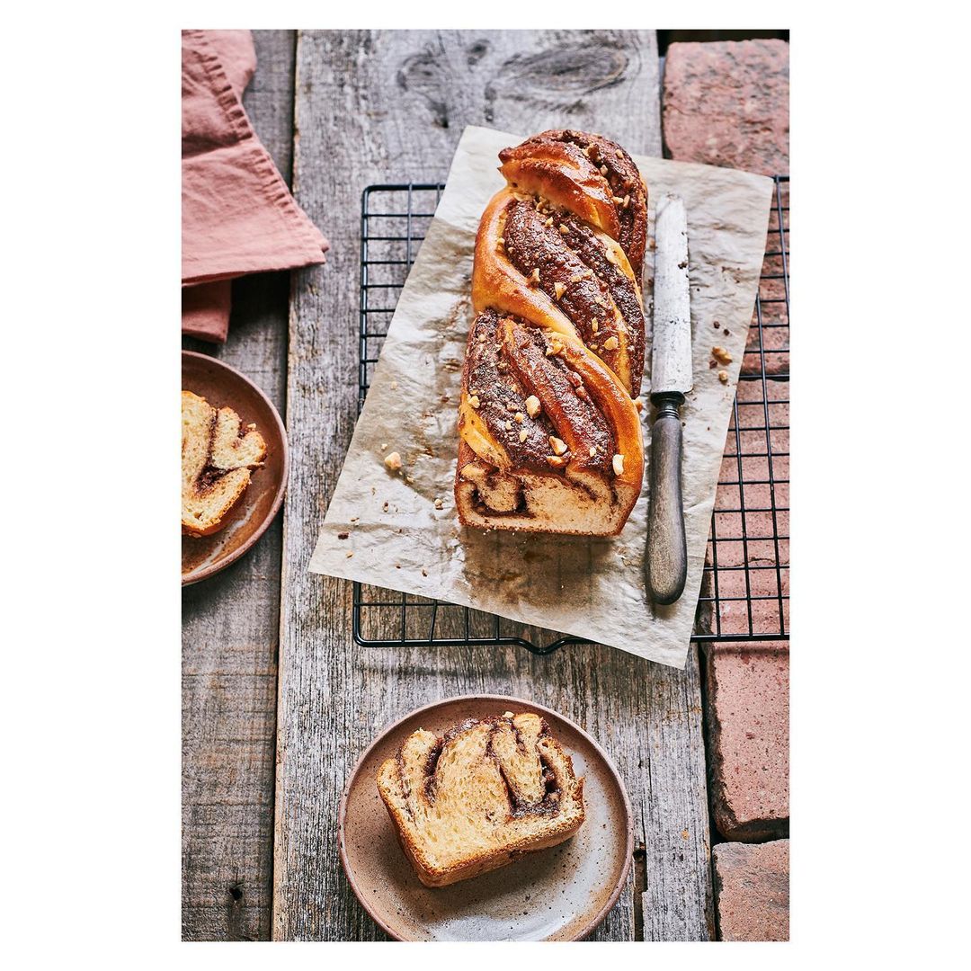 Overhead view of a chocolate babka loaf and slices on plates, arranged on a rustic wooden surface with a cooling rack and knife.