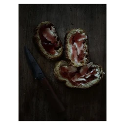 Sliced bread pieces topped with butter and red jam alongside a knife on a dark wooden surface in Paris by Laurent Moynat
