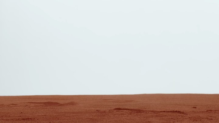 Minimalist landscape featuring a flat, arid terrain in reddish-brown hues against a stark white sky, creating a sense of desolation and simplicity.