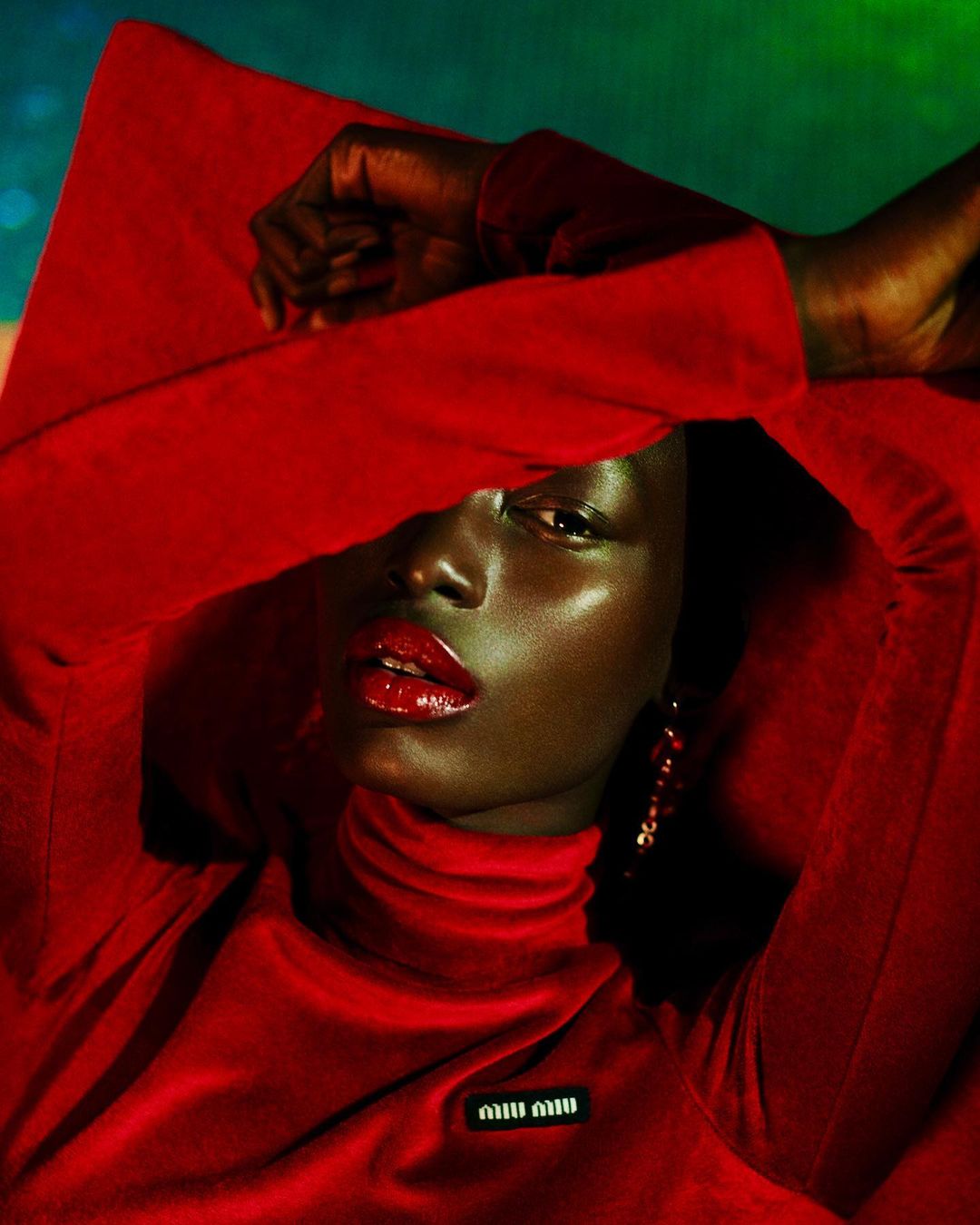 Portrait of a Black female model in a red turtleneck sweater and red lipstick, posing in a photo studio with a blurred background.