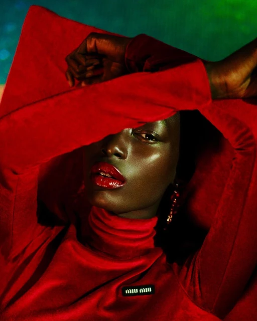 Portrait of a Black female model in a red turtleneck sweater and red lipstick, posing in a photo studio with a blurred background.