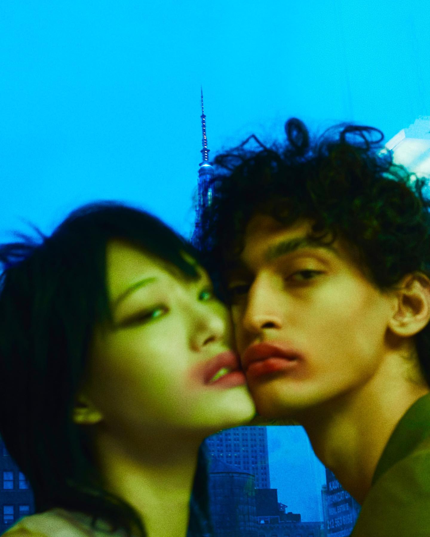 Close up of an adult couple with smeared lipstick posing in front of a city skyline with a bright blue sky background.