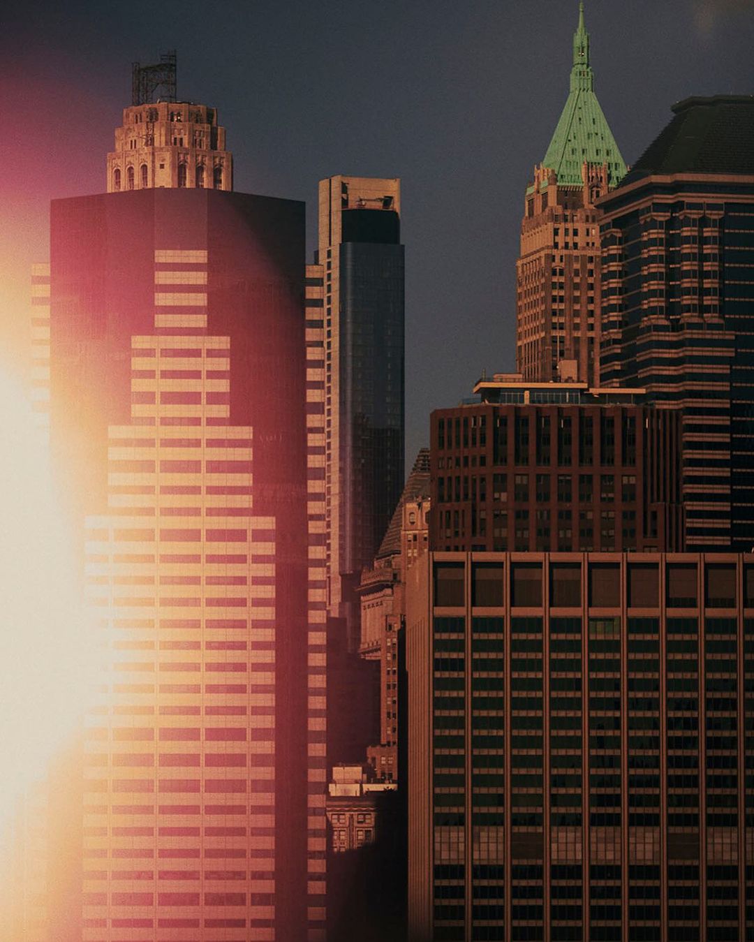 Skyscrapers in an urban cityscape with sun glare, showcasing architectural details and varied heights against a dark sky.