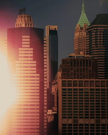 Skyscrapers in an urban cityscape with sun glare, showcasing architectural details and varied heights against a dark sky.