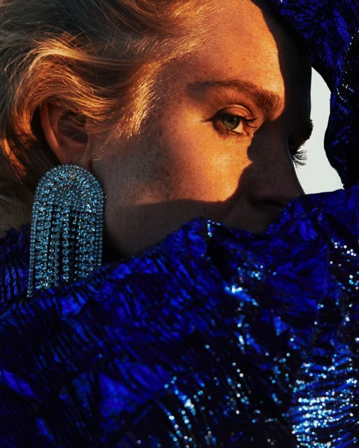 Close-up portrait of a fair-skinned woman in a sequined blue top and a large, jeweled earring. Her expression is neutral with shadow detail.