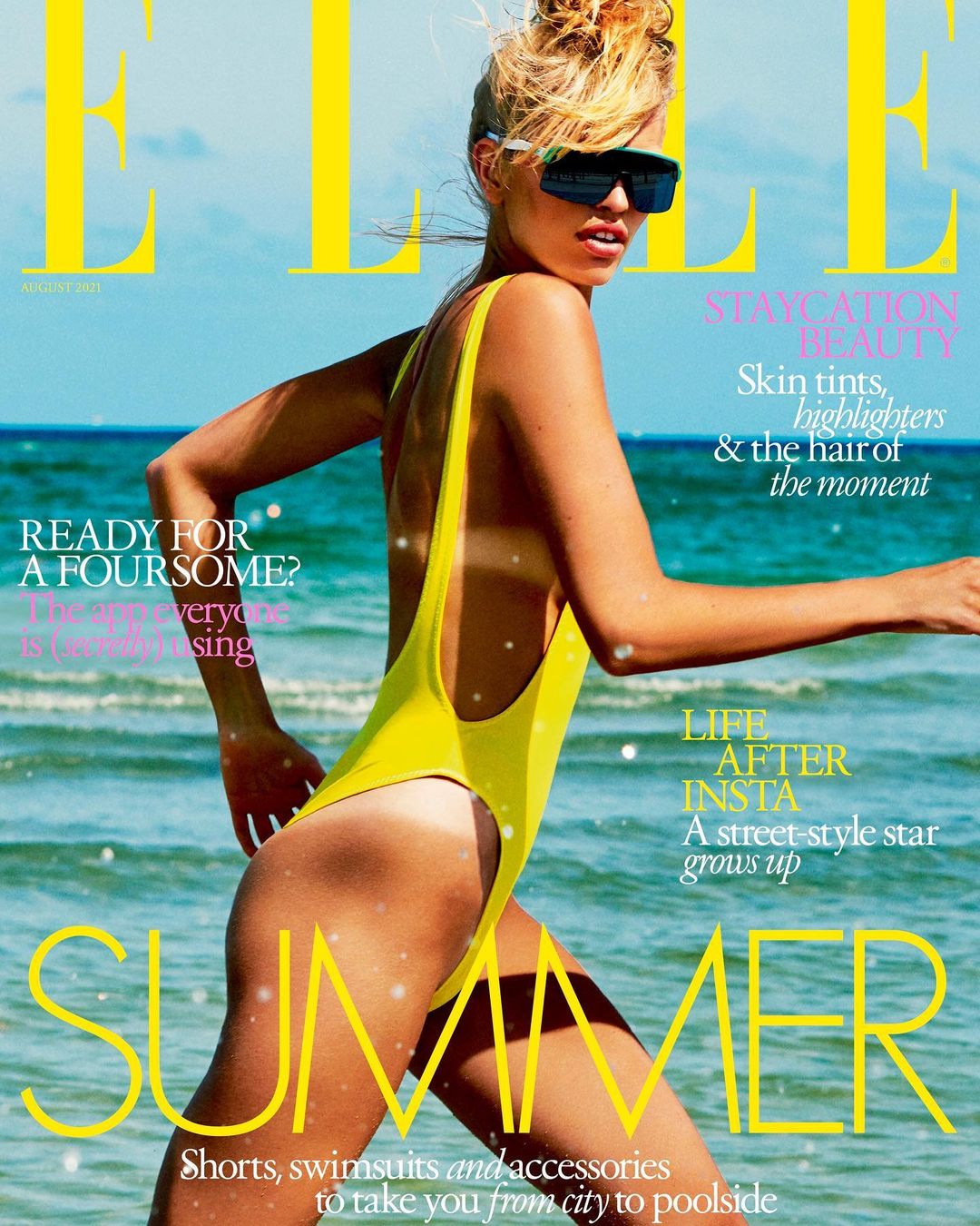 Elle magazine cover featuring a woman in a yellow swimsuit and sunglasses, standing on a beach with waves in the background on a sunny day.