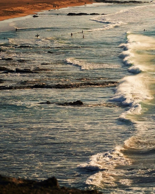 Seascape photo of crashing waves on a sandy shore with people in the distance, captured at eye-level in natural light.