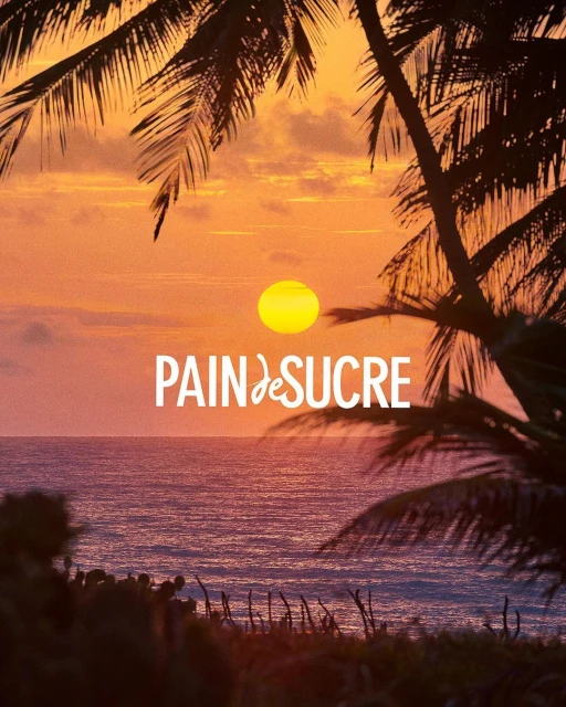 Sunset over the ocean with silhouetted palm trees framing the scene and 'Pain de Sucre' text overlayed over the horizon.