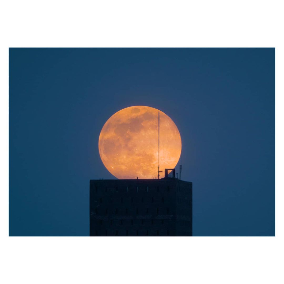 Full moon over a dark silhouette of a building against a dark blue sky, creating a striking and slightly mysterious celestial image.