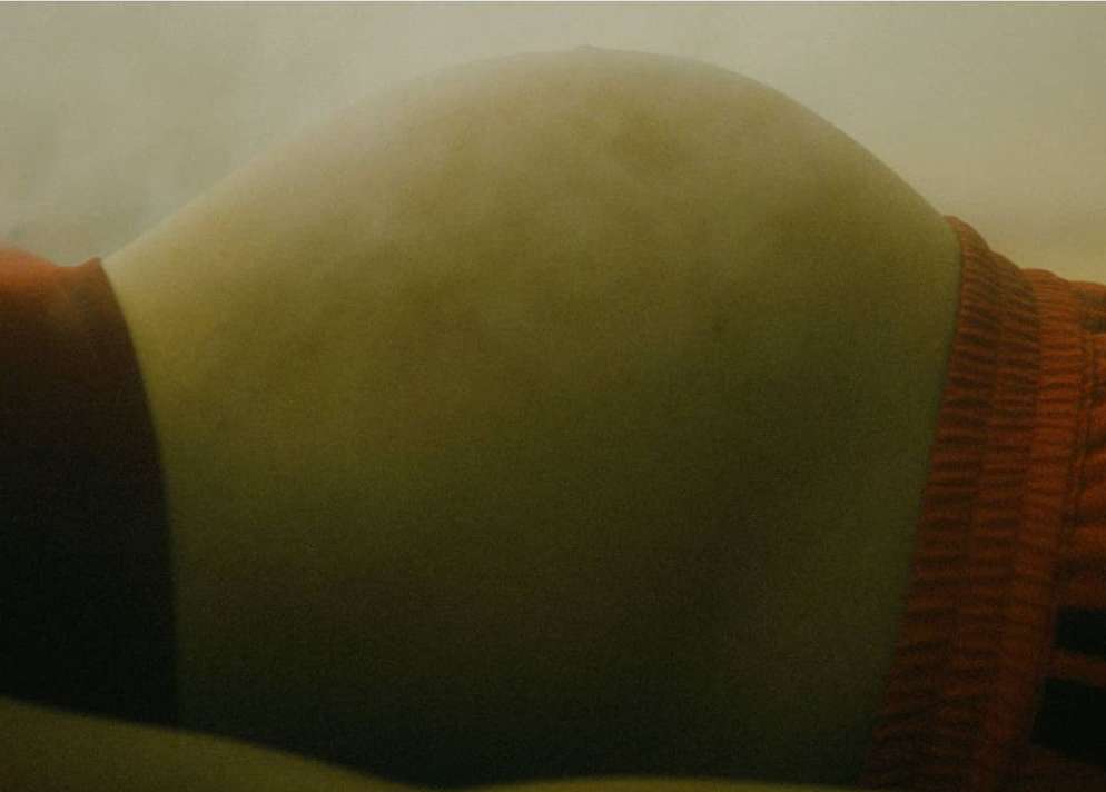 Close-up studio shot of pregnant abdomen with orange knitwear. Body casting and healthcare concepts are visually evoked.