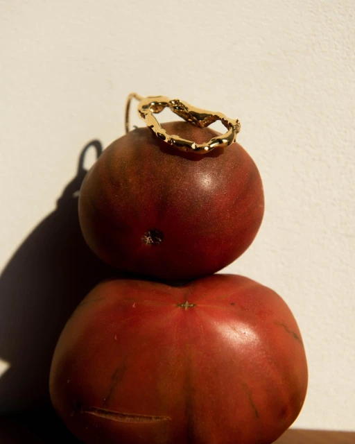 Gold ring displayed on a stack of two heirloom tomatoes in a studio setup with a neutral backdrop and soft, directional lighting.