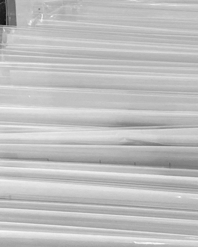 Black and white close-up showing an abstract composition of stacked, translucent sheets creating parallel lines and subtle textural patterns.