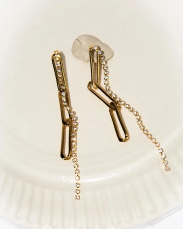 Close-up of gold chain earrings embellished with small clear rhinestones resting on a white surface