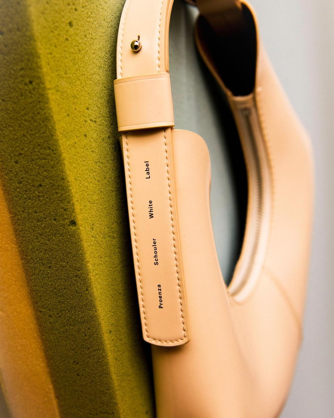 Close-up of a Proenza Schouler White Label handbag in a studio setting, showcasing its design and texture against a textured background.