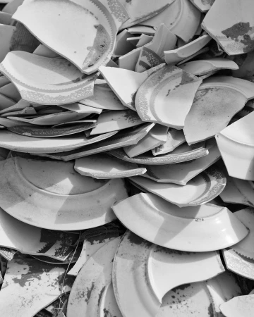 Close-up shot of a monochrome image showcases a disorganized pile of fragmented white plates, their pieces overlapping and scattered.