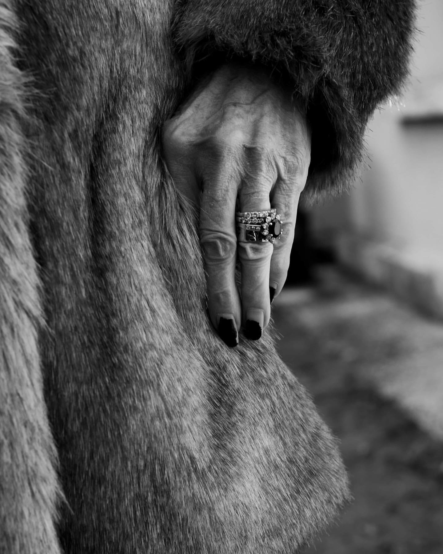 Black and white image of a hand adorned with rings resting on a furry coat, highlighting textures and jewelry.