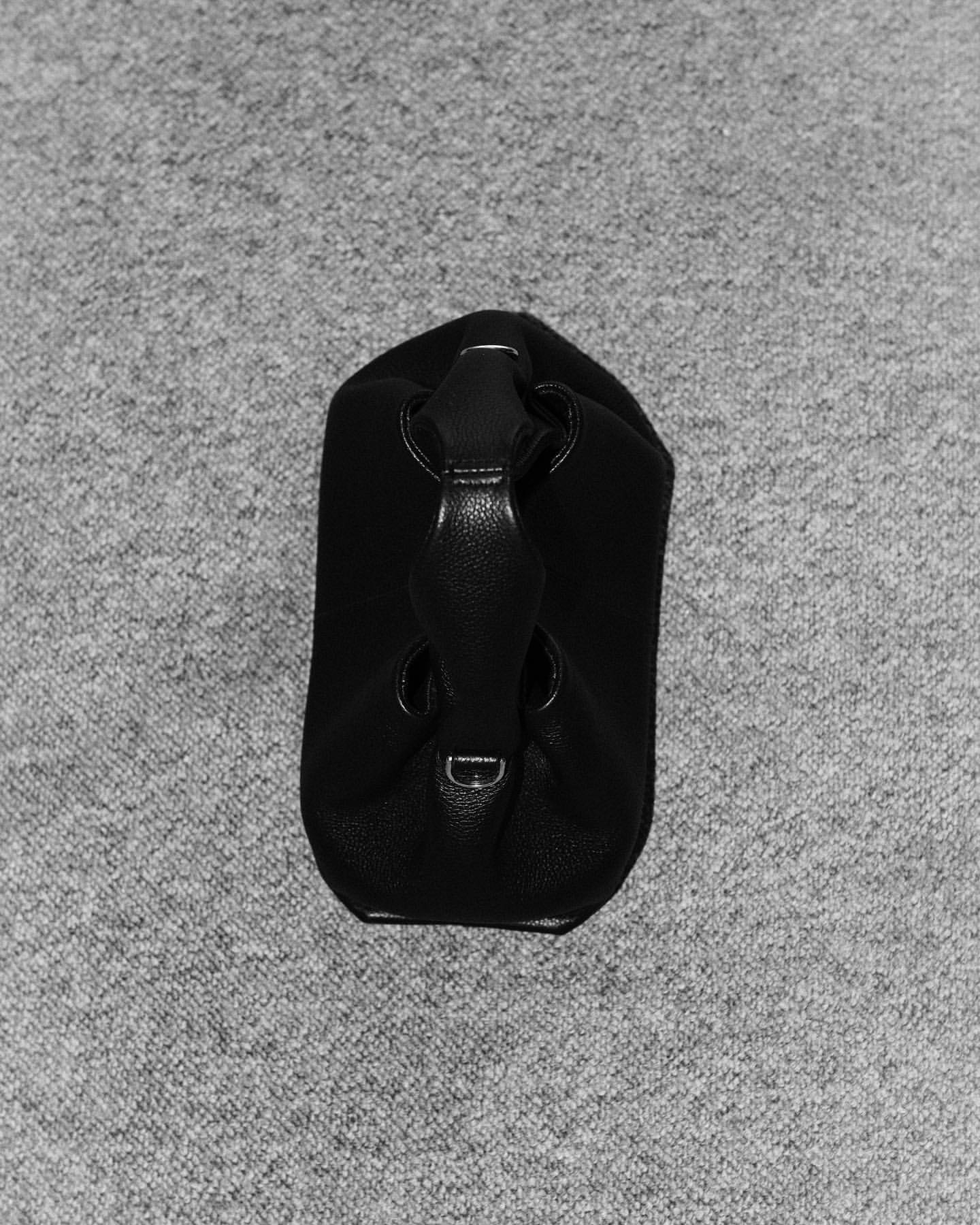 Black leather handbag resting upright on a textured grey carpet background