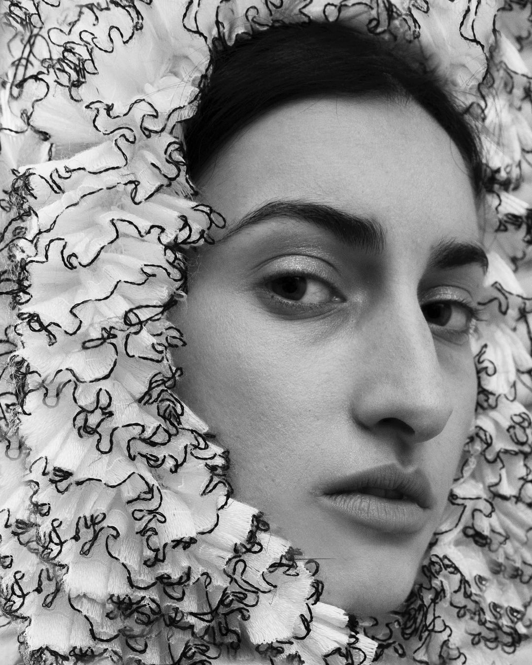 Monochrome portrait of a woman with a close-up shot, framed by a white ruffled collar with dark trim, creating a stark contrast.