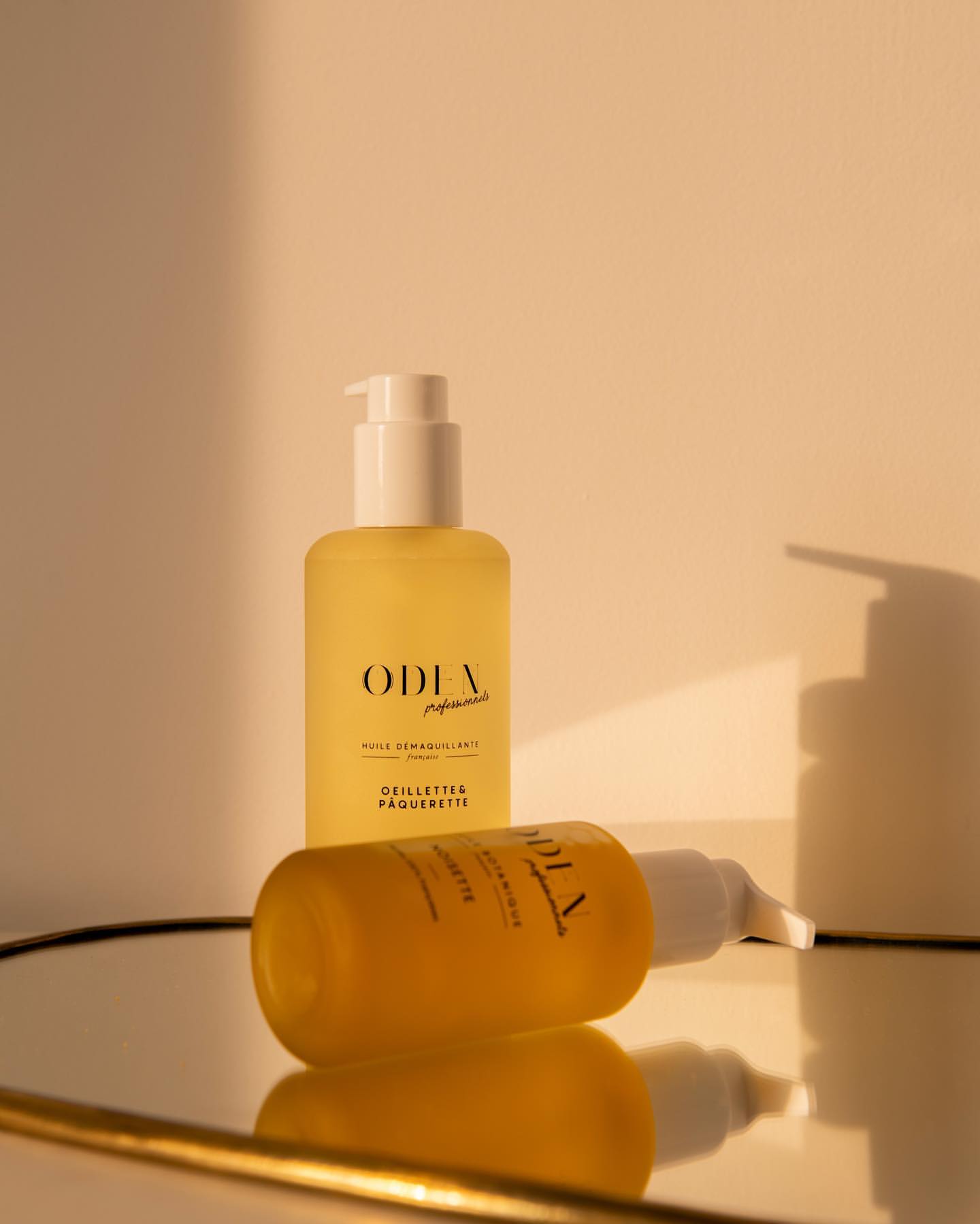 Two bottles of skincare product on a reflective surface with golden frame, bathed in warm, soft sunlight. Beauty product photography.