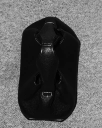 Overhead studio view of a black leather handbag with a top handle resting on a textured gray carpet.