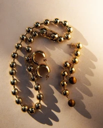 Close-up still life photograph of polished gold sphere jewelry and hoop earrings arranged on a light surface.