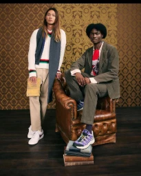 Two male models posing indoors with a vintage leather armchair and books, photographed by Lawrence Agyei