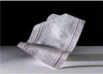 Intricate white paper sculpture with embossed floral patterns resting on a flat surface against a dark background.