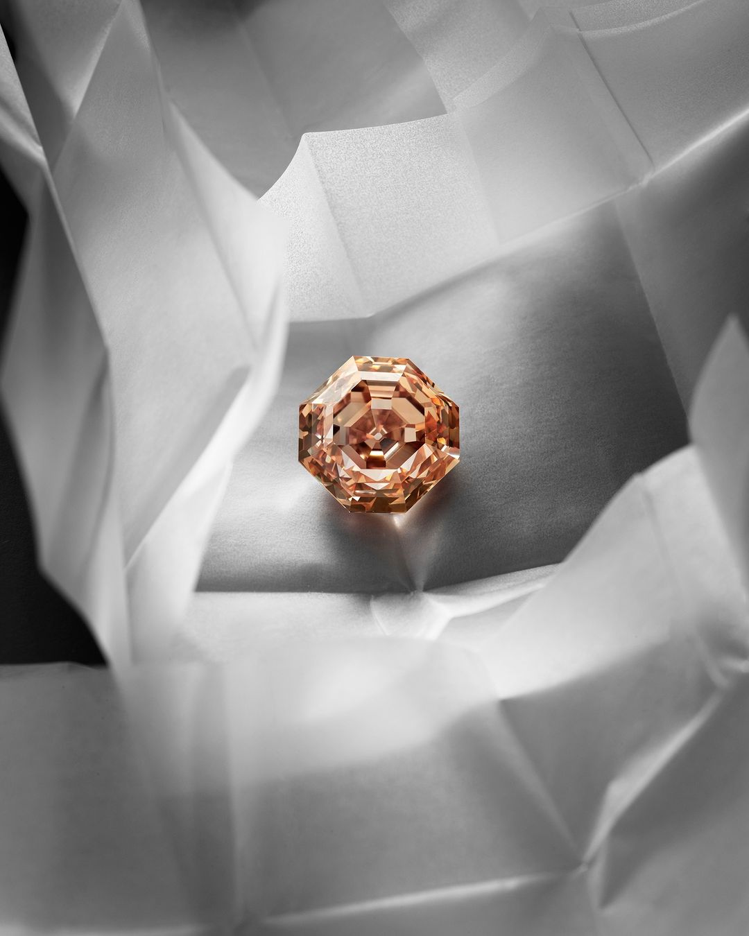 Close-up shot of a gemstone, cut in an octagonal shape, nestled on crinkled white fabric. The gemstone is in the center of the frame.