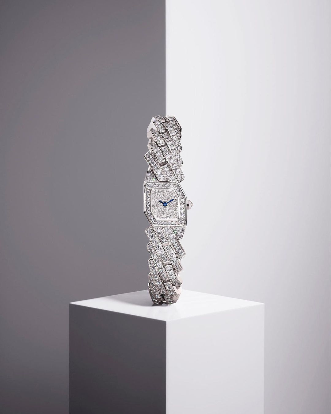 Elegant women's wristwatch made of platinum and diamonds displayed on a white cubic stand against a gray and white gradient background.