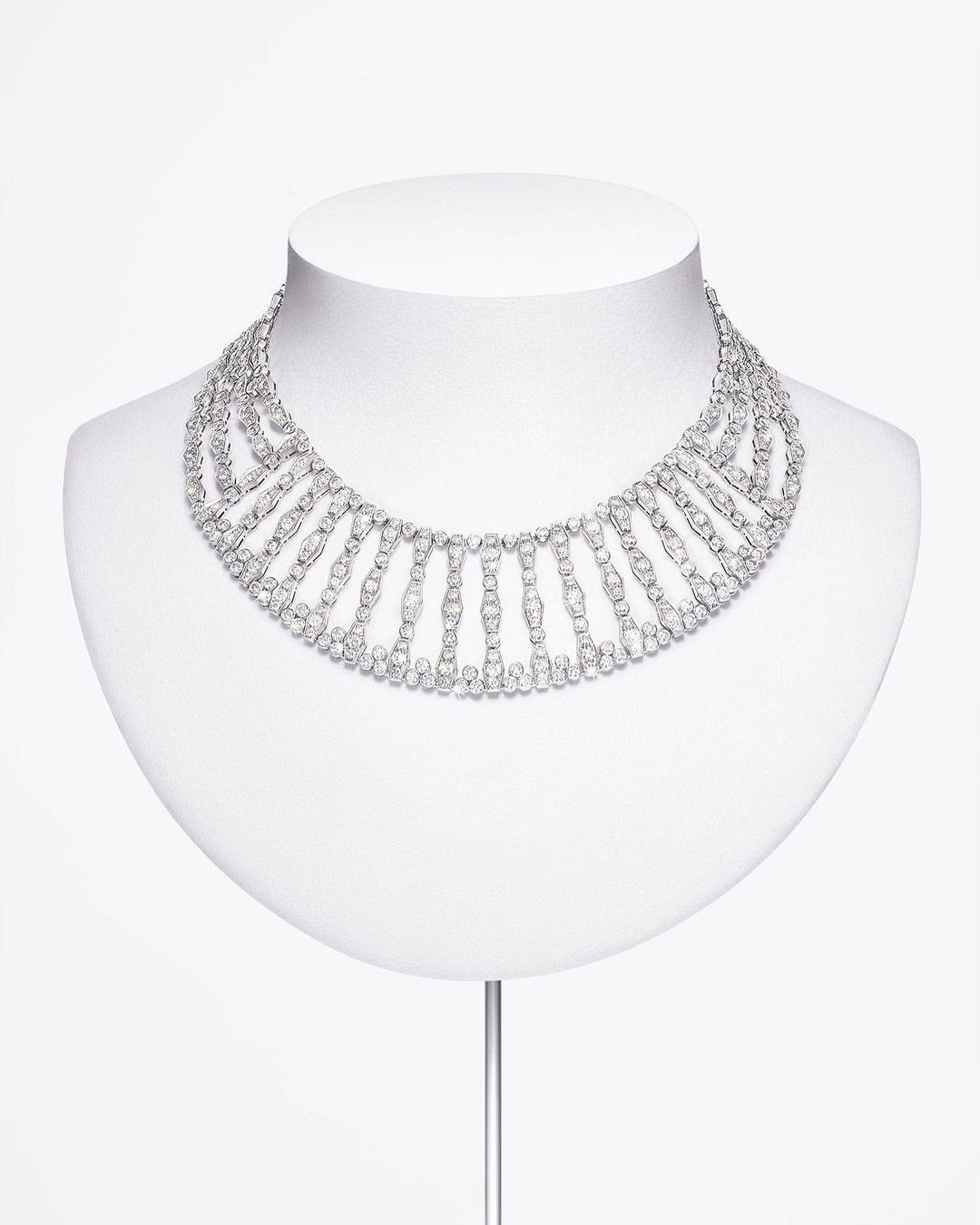 Statement necklace made of repeating, connected geometric shapes set with diamonds, displayed on a white mannequin against a white backdrop.