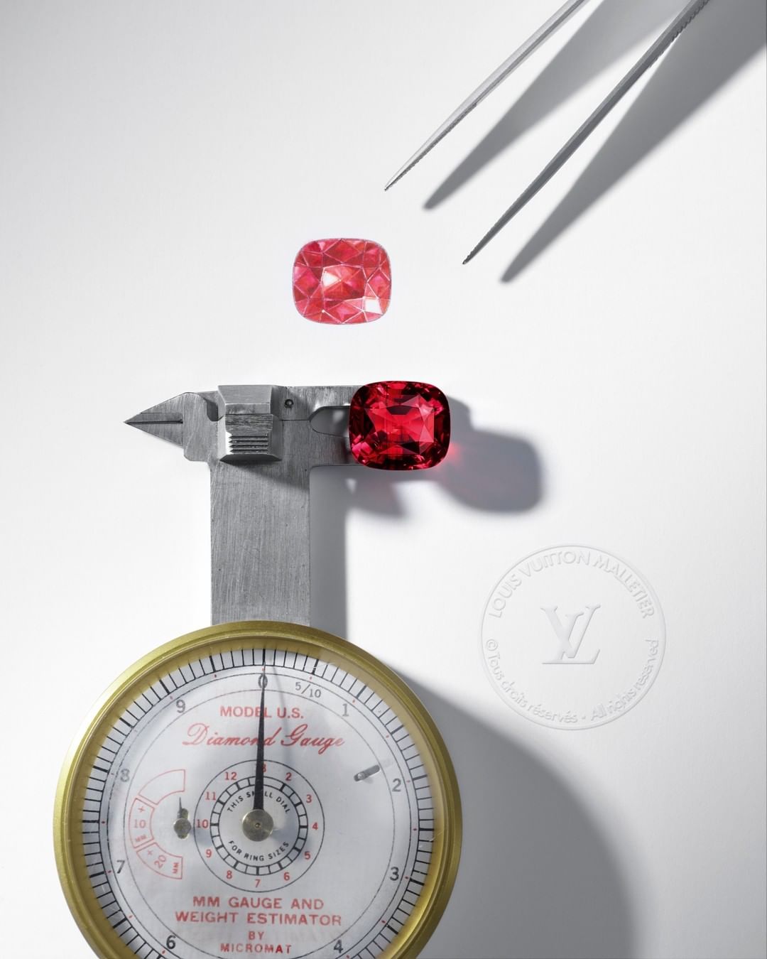 Cushion cut gemstone duo in red hues sit on a white background with a gauge and metal tweezers used in jewelry design and manufacturing.