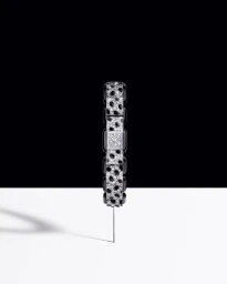 A diamond and black lacquer luxury watch balanced upright on a thin pin against a split black and white studio background.