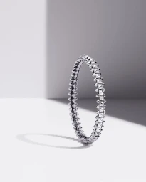 Silver studded bangle bracelet standing upright casting a shadow on a white surface.